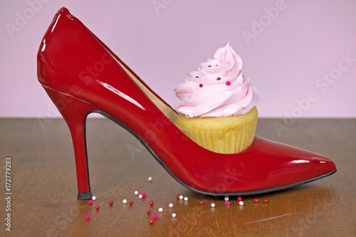 cupcake with pink frosting and sprinkles in red high heel shoe on wood