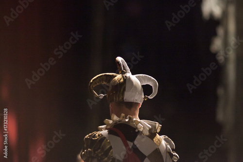 outfit, theater, excitement concept. back of young man dressed in costume of the court jester with funny fools cap and bright jacket with black and gold rhombuses