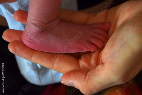 kleines Füsschen von einem neugeborenen Baby in der Hand der Mutter