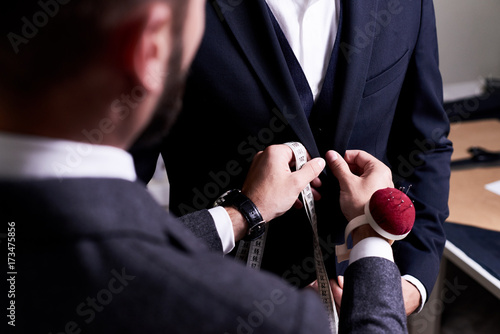 Over shoulder view of bearded fashion designer fitting bespoke suit to model, close-up shot