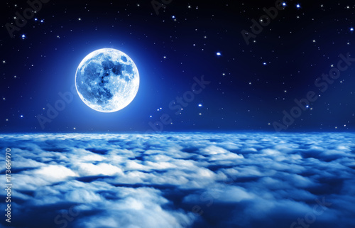 Bright full moon in a starry night sky above dreamy clouds with soft glowing light