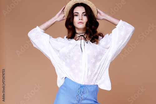 Sexy brunette woman wear short blue cotton short and silk summer collection blouse perfect body shape diet skin tan hold accessory hat glamour model fashion dress catalog clothes date party walk.