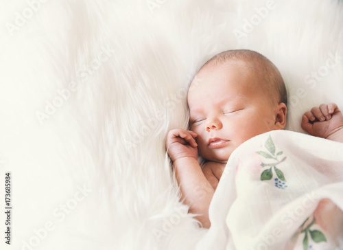 Sleeping newborn baby in a wrap on white blanket.