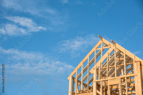 Close-up of gables roof on stick built home under construction and blue sky in Humble, Texas, USA. New build roof with wooden truss, post and beam framework. Timber frame house, real estate background