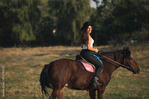 Beautiful young cowgirl riding her horse in field