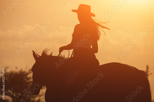 Zmierzch sylwetka młody cowgirl jedzie jej konia