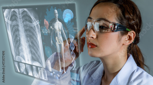 Young female doctor looking at hologram screen. Electronic medical record. Smart glasses. Medical technology concept.