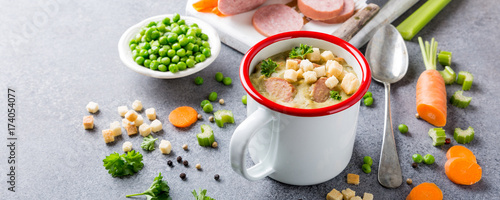 White enamel mug with delicious homemade pea soup with sausage and croutons. Healthy food concept.