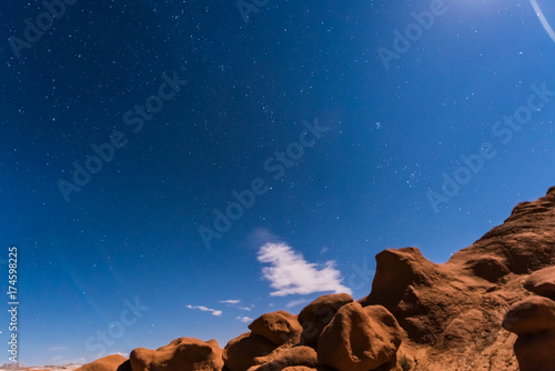 Night sky with full moon rising, or moonrise, in Goblin Valley State Park in Utah showing clouds, stars, and canyons silhouettes in wilderness nature