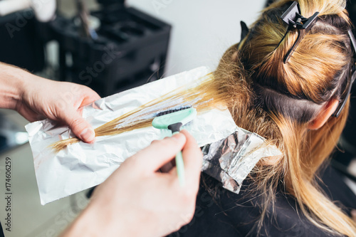 Hairdresser is dying female hair, making hair highlights to his client with a foil. 