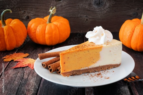 Slice of pumpkin cheesecake with whipped cream on a dark rustic wood background