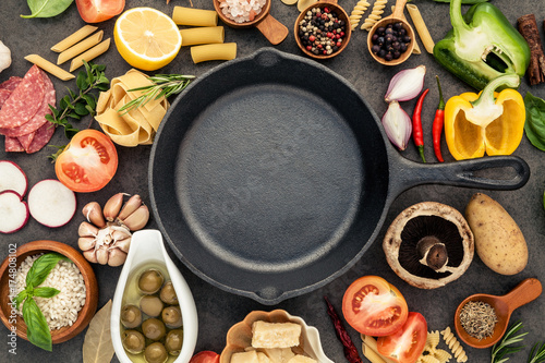 Italian food cooking ingredients on dark stone background with cast iron pan flat lay and copy space.