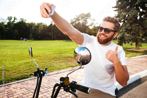 Smiling bearded man in sunglasses sitting on modern motorbike