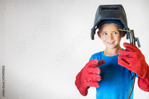 Happy little kid in welder mask and welding equipment. Welding equipment, welding mask, protective leather gloves, welding electrodes. Fun concept. Child dreaming of future profession. Career choice. 