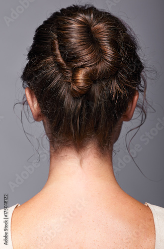 Head and shoulders of a young woman from the back side. Female hair knotted