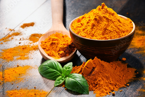 Composition with bowl of turmeric powder on wooden table