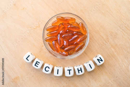 Lecithin gel pills in a round glass bowl and with the word Lecetin from the letters of cubes on a light wooden background. Soy and sunflower lecithin benefits for skin, digestion, lower cholesterol.