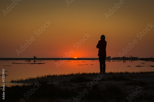 The sun dips below the horizon as an onlooker watches