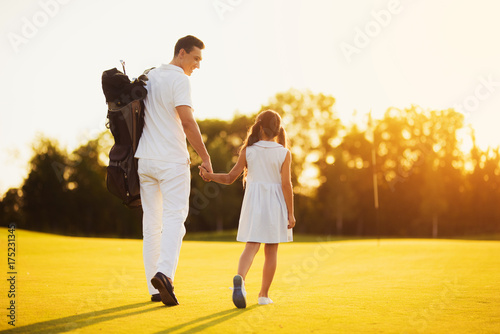 Father and daughter walking against the sunset over the golf course. They are turned with their backs towards the camera