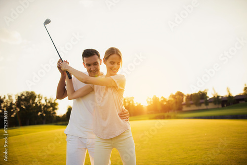 A man is teaching his girlfriend how to play golf at sunset