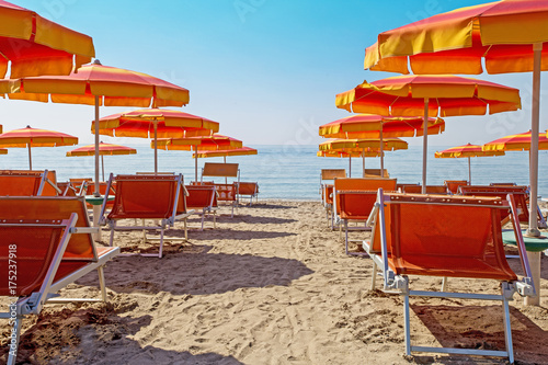 Orange beach umbrellas and couches on blue sky and sea background on the beach of Milano Marittima, Adriatic coast, Italy. Popular Tourist Resort at Adriatic Sea