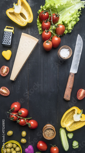 Preparation of salad with tomatoes, olives, butter and various seasonings, ingredients are lined around the cutting board on a blue wooden background
