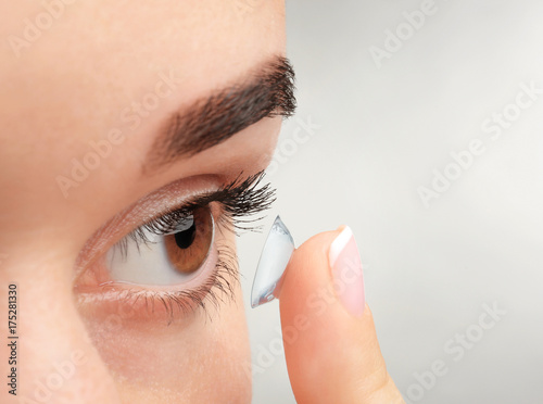 Young woman putting contact lens on light background, closeup