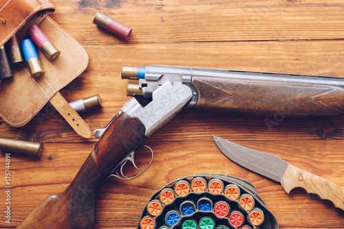 Hunting equipment. Shotgun, hunting cartridges and hunting knife on wooden table.