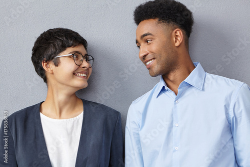 Close up portrait of interracial business couple dressed formally, look with happy expressions at each other, rejoice successful signed contract, have triumph. Mixed race relationship, career concept