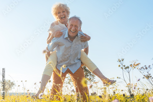 Senior Mann trägt seine Frau auf dem Rücken, er hat eine gesunde Wirbelsäule