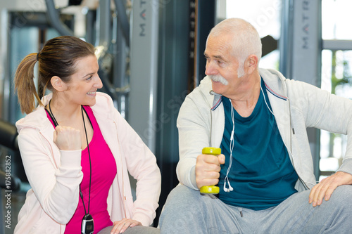 happy physiotherapist assisting senior man in lifting dumbbells