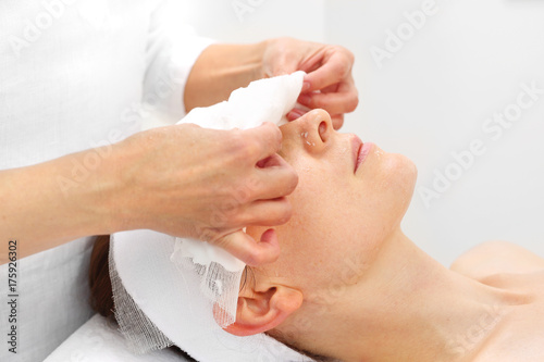 Pielęgnacja skóry w klinice medycyny estetycznej. Kosmetyczka zdejmuje pacjentce bandaż z twarzy.