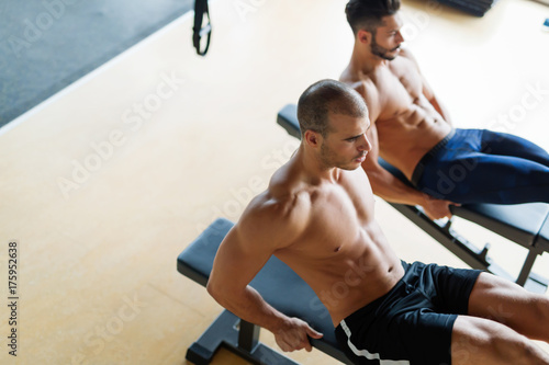 Strong men are doing abs crunches on bench