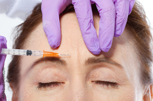 Forehead of middle age woman and doctor giving injection