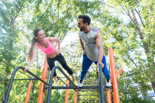 Low-angle view of a young fit woman and her partner smiling while practicing plank exercise during outdoor couple workout in a calisthenics park