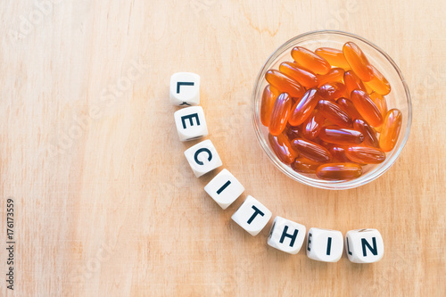 Lecithin gel pills in a round glass bowl and with the word Lecetin from the letters of cubes on a light wooden background. Soy and sunflower lecithin benefits for skin, digestion, lower cholesterol.