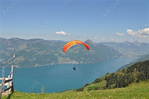Gleitschirmfliegen über dem Vierwaldstättersee inmitten der Schweizer Berge in der Zentralschweiz / Bunter Paragleiter / Gleitschirm fliegt über den See, Schweiz