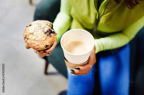 Young brunette woman drinking coffee and eating a delicious muffin cake in modern airport cafe, fastfood travel concept