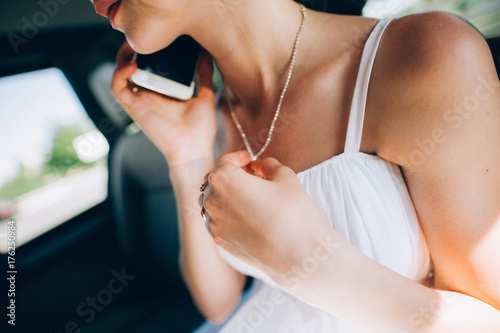 Girl in a white dress with a beautiful silver chain around her neck Stylish fashionable diamond suspension the girl speaks by phone a young woman holds a white phone in her hands