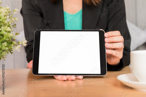 Businesswoman in black suit showing white screen digital tablet on desk.