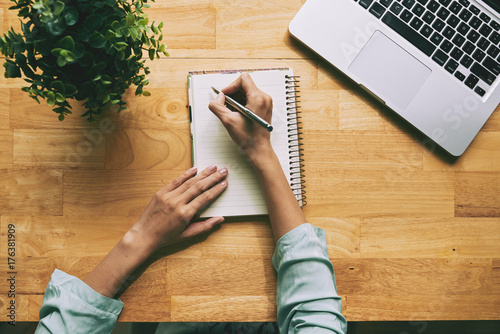 High angle view of unrecognizable businesswoman taking necessary notes in notepad while preparing for important meeting at modern office