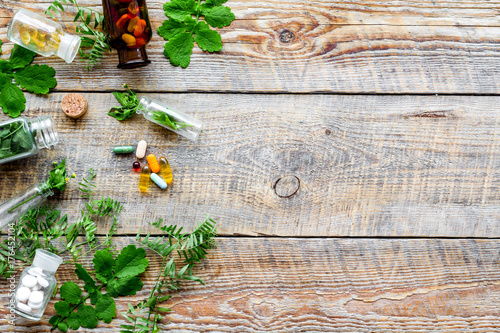 Healing herbs. Fresh leaves, bottles and pills on wooden background top view copyspace