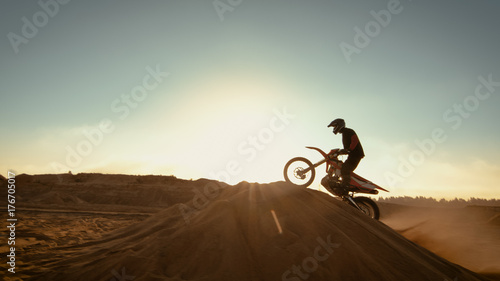 Professional Motocross Motorcycle Rider Jumping Over the Dune and Further Down the Off-Road Track. Shot on Deserted Quarry while Sun is Setting.