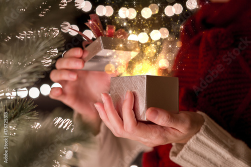 Female open Christmas gift box with gold ray of magic light on bokeh lights background.