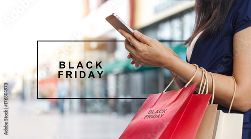 Black Friday, Woman using smartphone and carrying shopping bag while standing on the mall background