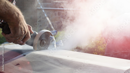 Construction worker cutting concrete plate for fence fundation using a cut-off saw.