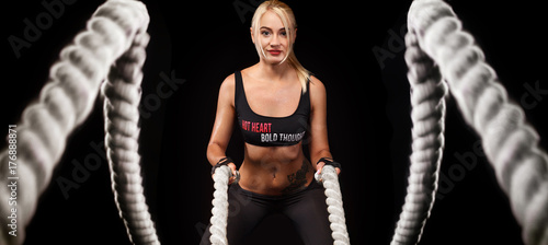 Battle ropes session. Attractive young fit and toned sportswoman working out in functional training gym doing crossfit exercise with battle ropes. Fitness and workout motivation