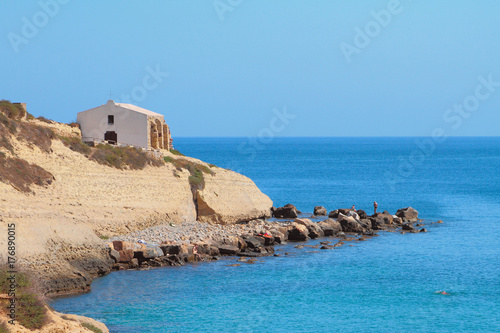 Sea, rocky coast and church. Porto-Torres, Italy