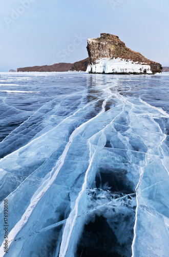 Baikal Lake in February. Olkhon Island. View from the smooth blue ice with cracks on the cape of Horin-Irgi, which locals call the Horse's Head (Kobylia Golova). Focus on the ice