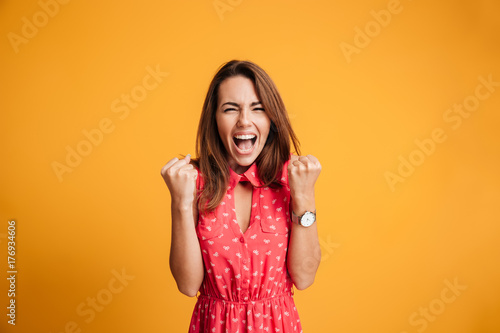 Close-up of emotional brunette woman keeping hands in fists, screaming while celebrating win